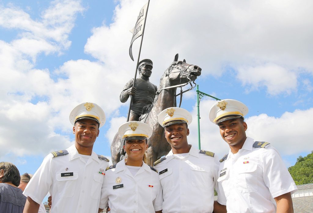 Four military cadets stand in front of a monument